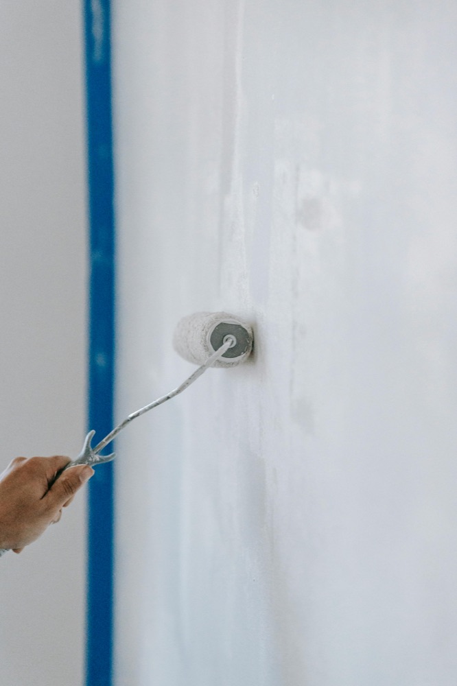 Hand streicht weiße Wand mit Farbroller